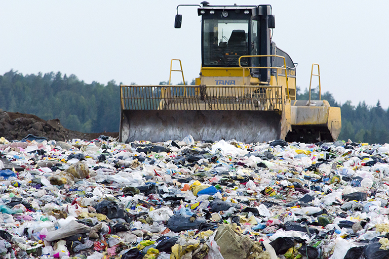 A bulldozer on top of a large pile of trash.