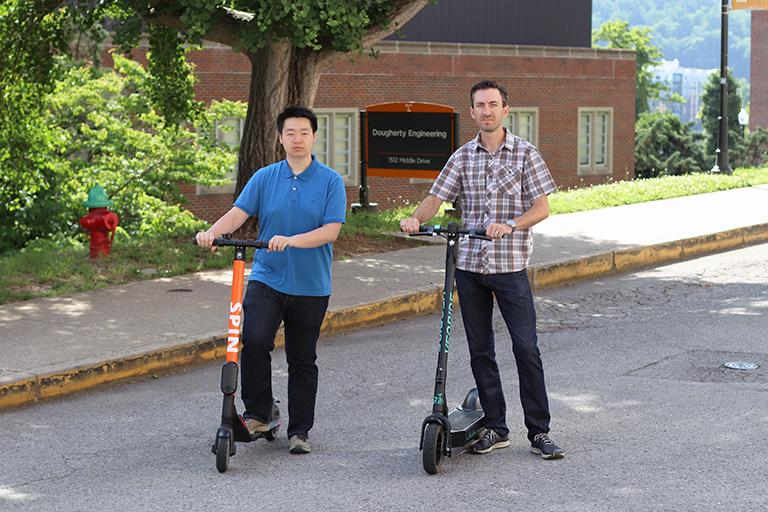 Chris Cherry and Yi Wen stand beside e-scooters in front of Dougherty Engineering Building.