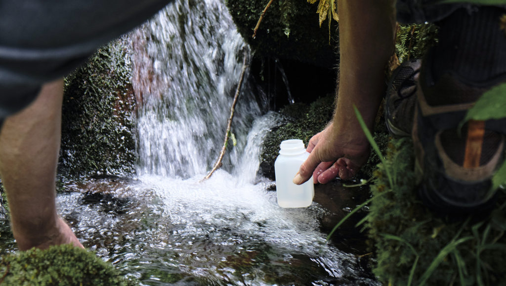 Disembodied arm uses a plastic bottle to collect water from a stream.