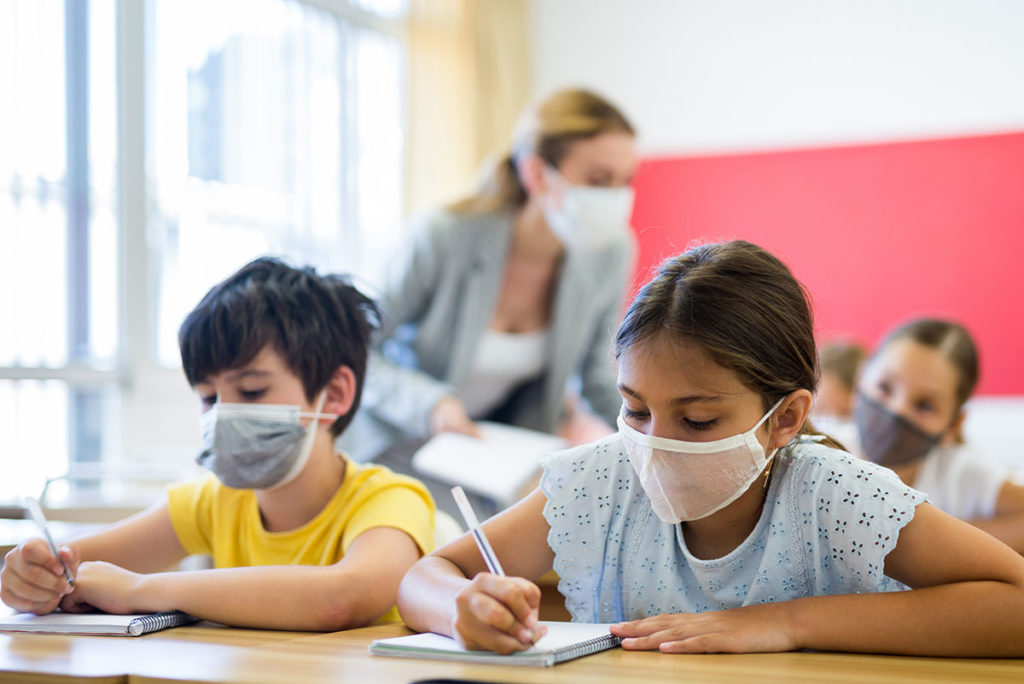 Two elementary students wearing masks sit at a desk.