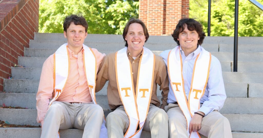 Triplet brothers Walker, Jackson, and Grey Reeves sitting on steps wearing their graduation sashes