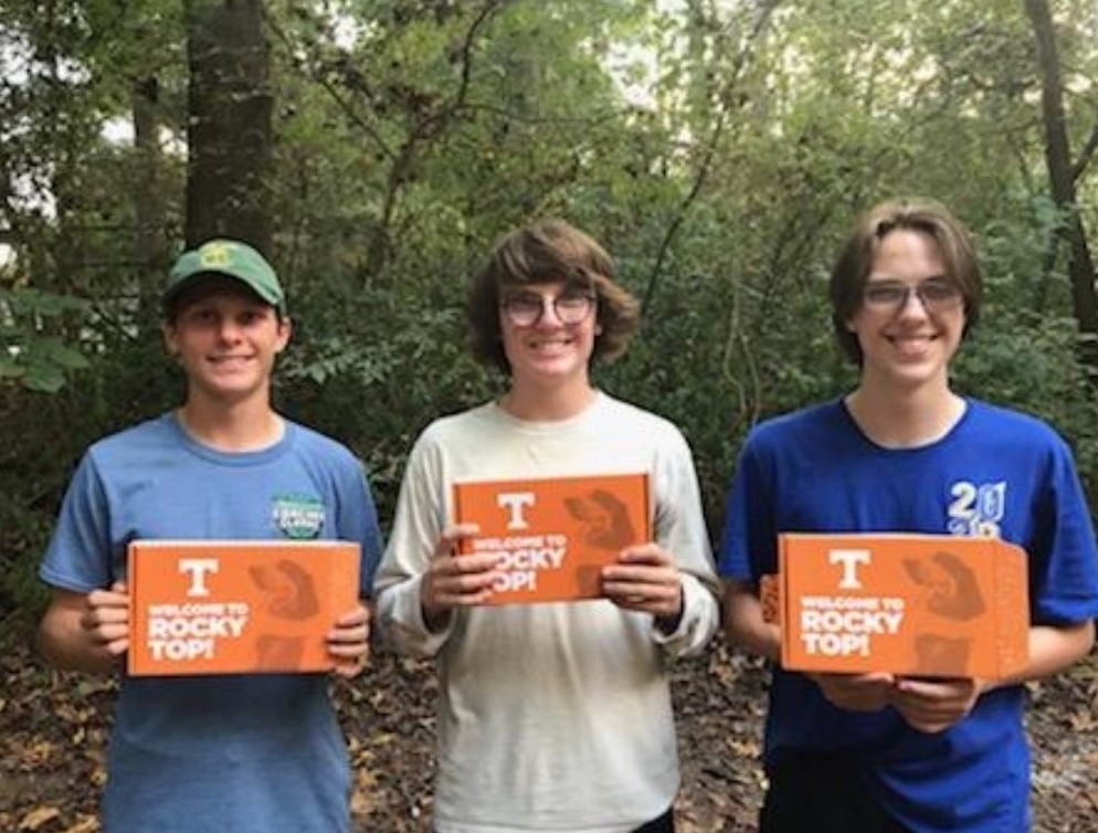 Walker, Jackson, and Grey Reeves holding their University of Tennessee admission boxes in the woods