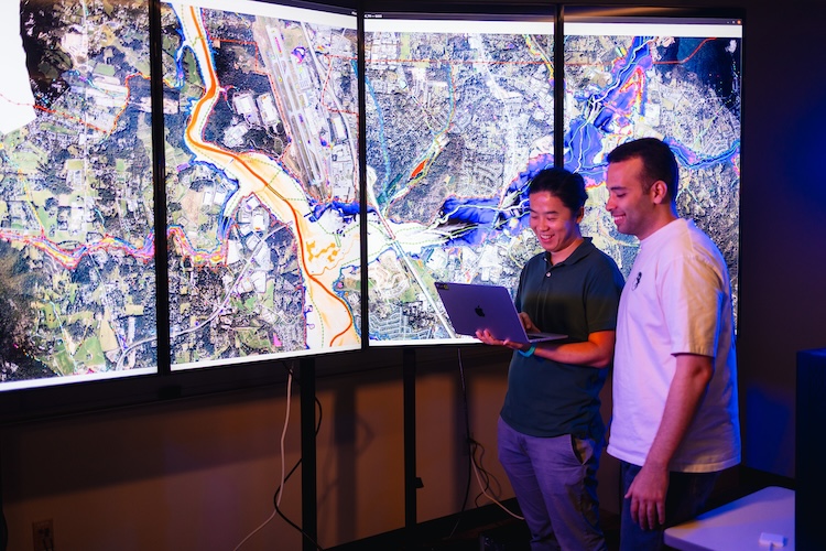 Haochen Li and another professor looking at flood modeling on monitors